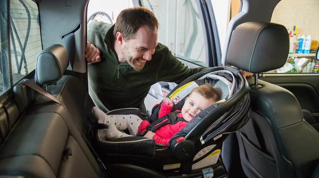 Parent buckling an infant into a car seat in the back seat of a vehicle